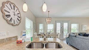 A modern kitchen with a granite countertop, stainless steel sink, and a large wall clock. - Family-Friendly Waterfront Paradise! (Holmes Beach)