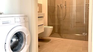 Une salle de bain moderne équipée d’un lave-linge, de toilettes et d’une douche à parois de verre.