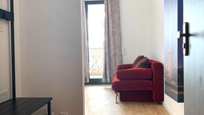 Une pièce avec un plancher en bois, un canapé rouge, un bureau noir et une porte dotée d’un cadre bleu.