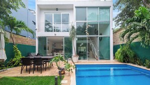 Une maison moderne à deux étages, dotée d’une piscine, d’un espace extérieur aménagé et d’un escalier menant à l’étage supérieur.