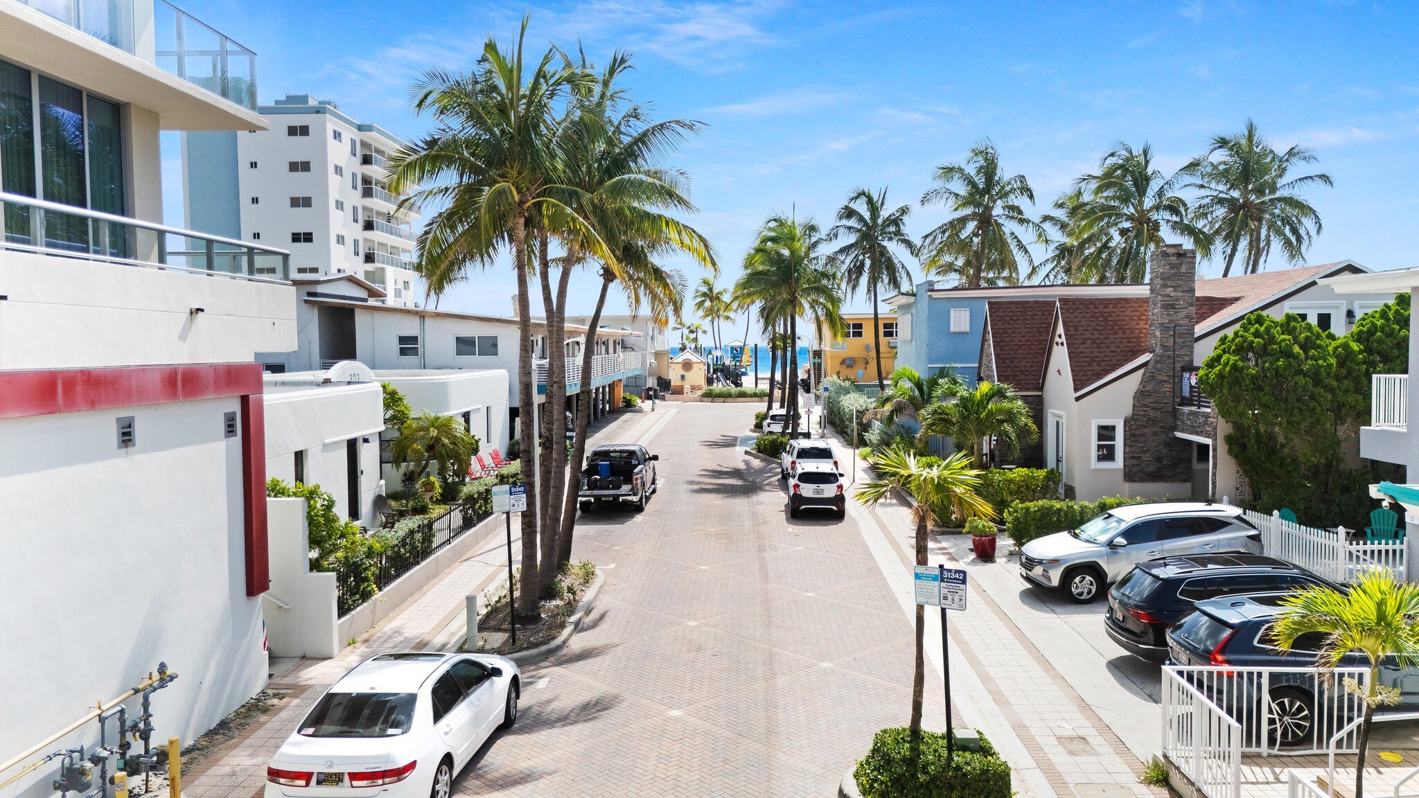 A residential street lined with palm trees and parked cars.