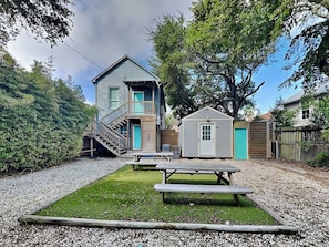 Una casa de dos pisos con balcón, un cobertizo pequeño y una mesa de picnic en el jardín.