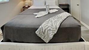 Una cama bien hecha con un edredón gris, una manta blanca y dos toallas dispuestas en forma de cisne.