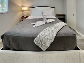 A neatly made bed with a gray quilt, a white throw blanket, and two towels arranged in a swan shape on the bed. - Pleasure Pier Retreat #3 | Fenced Backyard & Great Location (Galveston)