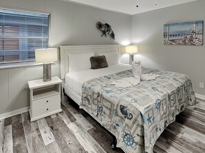 A bedroom with a bed, bedside tables, a lamp, a painting, and a window with blinds.