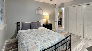 Een slaapkamer met een bed, nachtkastje, plafondventilator en een deur naar een andere kamer.