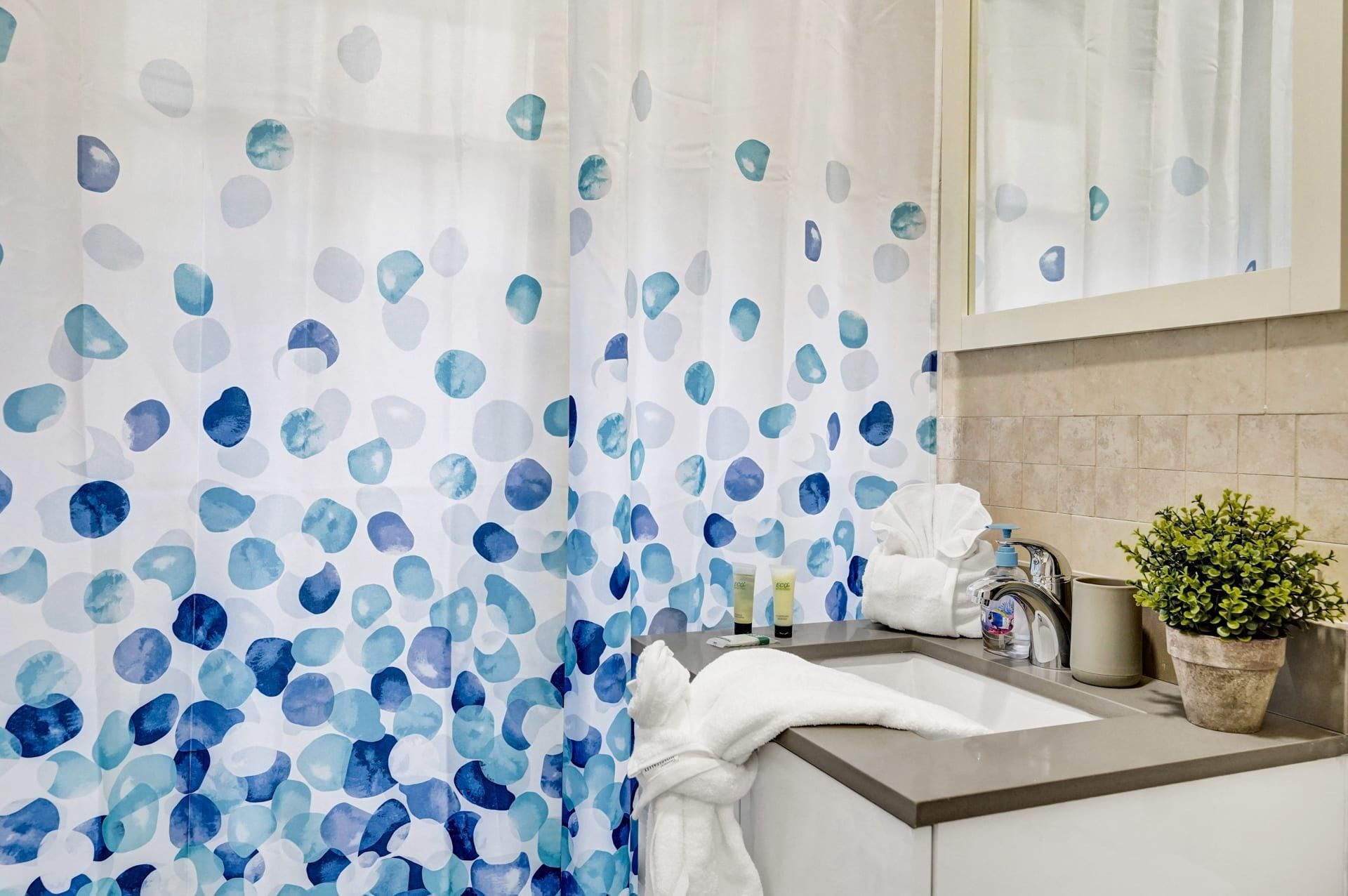 A bathroom with a shower curtain featuring blue and white abstract patterns, a sink with toiletries, and a potted plant.