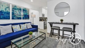 A modern living room with a blue sofa, a glass coffee table, and abstract art on the wall. - Newly Renovated Apt-unit #1 Close to Beach (Hollywood)