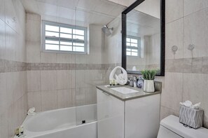 Ein modernes Badezimmer mit einer Badewanne, einem Waschbecken mit Toilettenartikeln, einem Spiegel und einem Fenster.