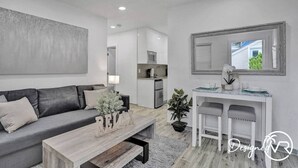 Un salon moderne avec un canapé gris, une table basse en bois et un bureau blanc agrémenté d’un miroir.
