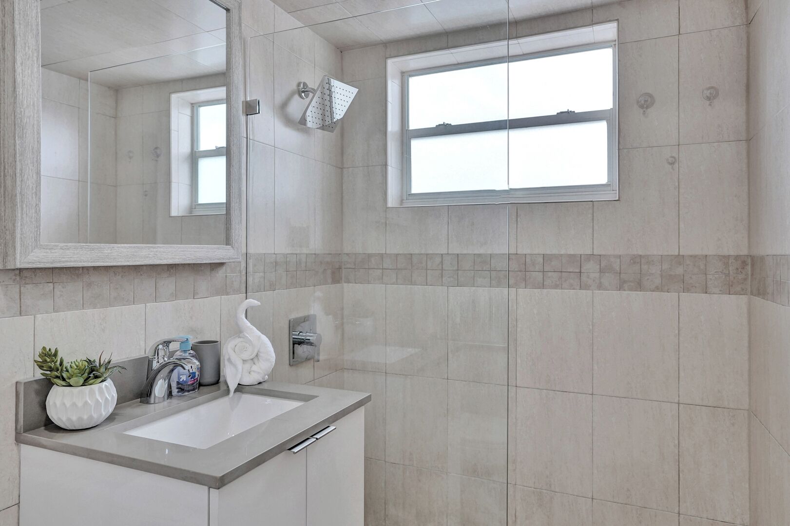 A modern bathroom with a large mirror, a showerhead, and a window.