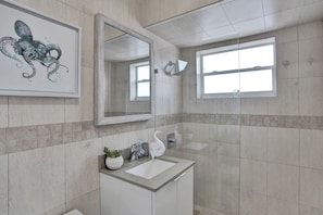 Un baño moderno con un espejo grande, un lavamanos y una ventana.