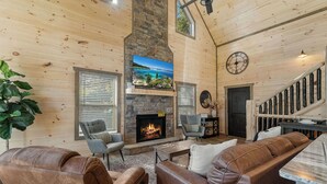 A cozy living room with a stone fireplace, leather sofas, and a large TV screen.