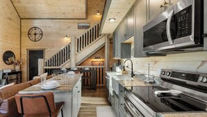 A modern kitchen with a central island, stainless steel appliances, and a wooden staircase.