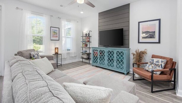 Una sala de estar moderna con un sofá seccional gris, un mueble de entretenimiento color turquesa y un ventilador de techo.