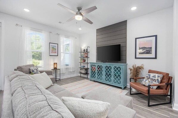 A modern living room with a grey sectional sofa, a teal entertainment unit, and a ceiling fan.