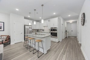 A modern kitchen with white cabinets, a central island with stools, stainless steel appliances, and pendant lighting. - Birdie Bungalow- Games, Beach Gear, Sleeps 10 (North Myrtle Beach)