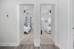 A hallway leading to a bedroom with a ceiling fan, a bed, and a window with curtains.