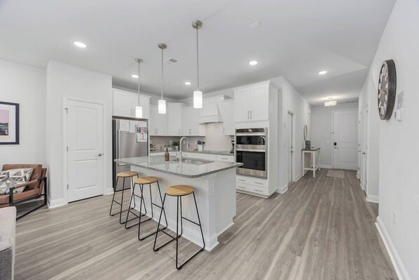 A modern kitchen with white cabinetry, a central island with stools, and built-in appliances.