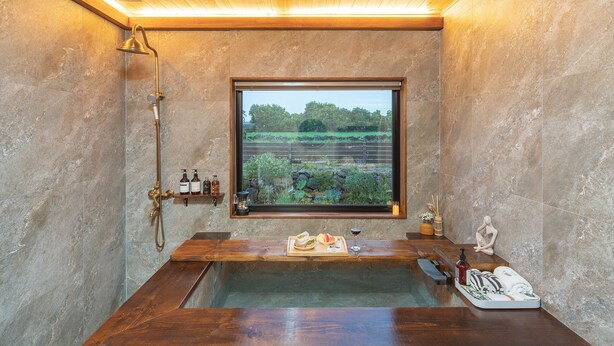 Een badkamer met een houten badkuip, een douche en een raam met uitzicht op groen.