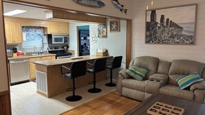 Eine moderne Küche mit Kochinsel, Barhocker und Essbereich mit Sofa und Couchtisch.