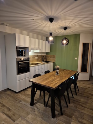 A modern kitchen with white cabinets, a built-in oven, and a wooden dining table with black chairs. - Apartment Tignes (Tignes)