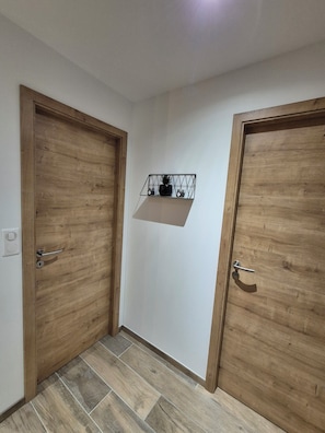 A hallway with two wooden doors, a metal shelf with decorative items, and a tiled floor. - Apartment Tignes (Tignes)