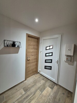 A hallway with a wooden door, a white door with black panels, and a shelf with decorative items. - Apartment Tignes (Tignes)