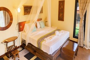 A bed with a canopy, a bedside table, a small stool, a mirror, and artwork on the walls.