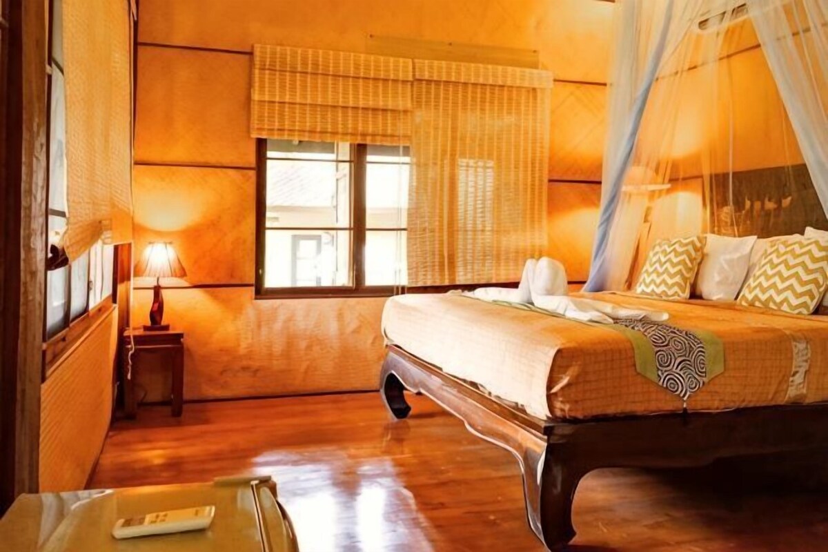 Une chambre à coucher avec un lit, une table de chevet, une lampe, une fenêtre avec des rideaux et une vue sur l’extérieur.