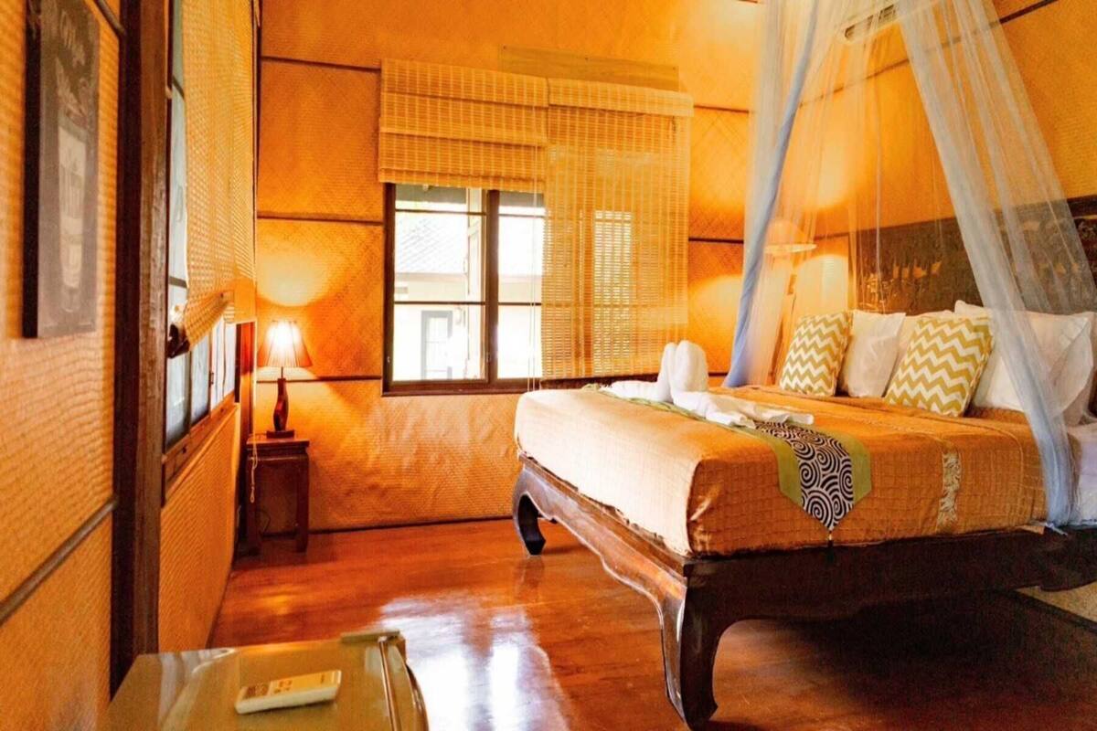 A bedroom with a bed, bedside table, lamp, and window with blinds.