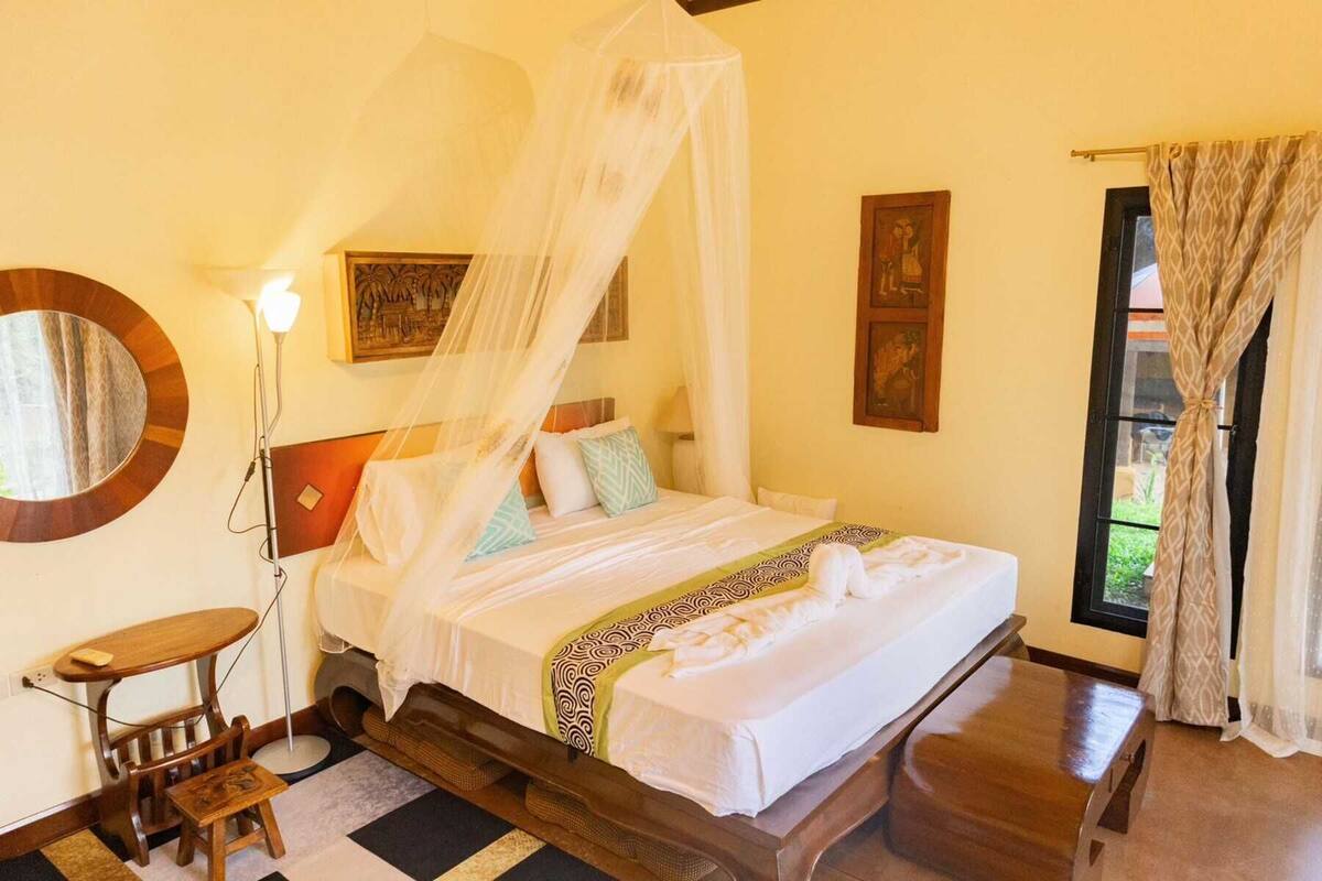 A room with a bed, a bedside table, a lamp, and a window with curtains.