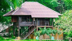 A wooden house with a corrugated metal roof, a staircase leading to a balcony, and surrounded by lush greenery. - Palette Luxe Elephant Camp Maerim (Mae Rim)