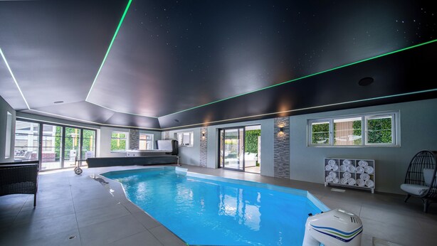 An indoor swimming pool with a ceiling that simulates a starry night sky, large windows, and a seating area with a poolside chair. - 22-guest luxury stay with Pool & Bar (Lytham St Annes)