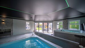 A modern indoor pool area with a hot tub, a stone wall, and a view of the outside. - 22-guest luxury stay with Pool & Bar (Lytham St Annes)