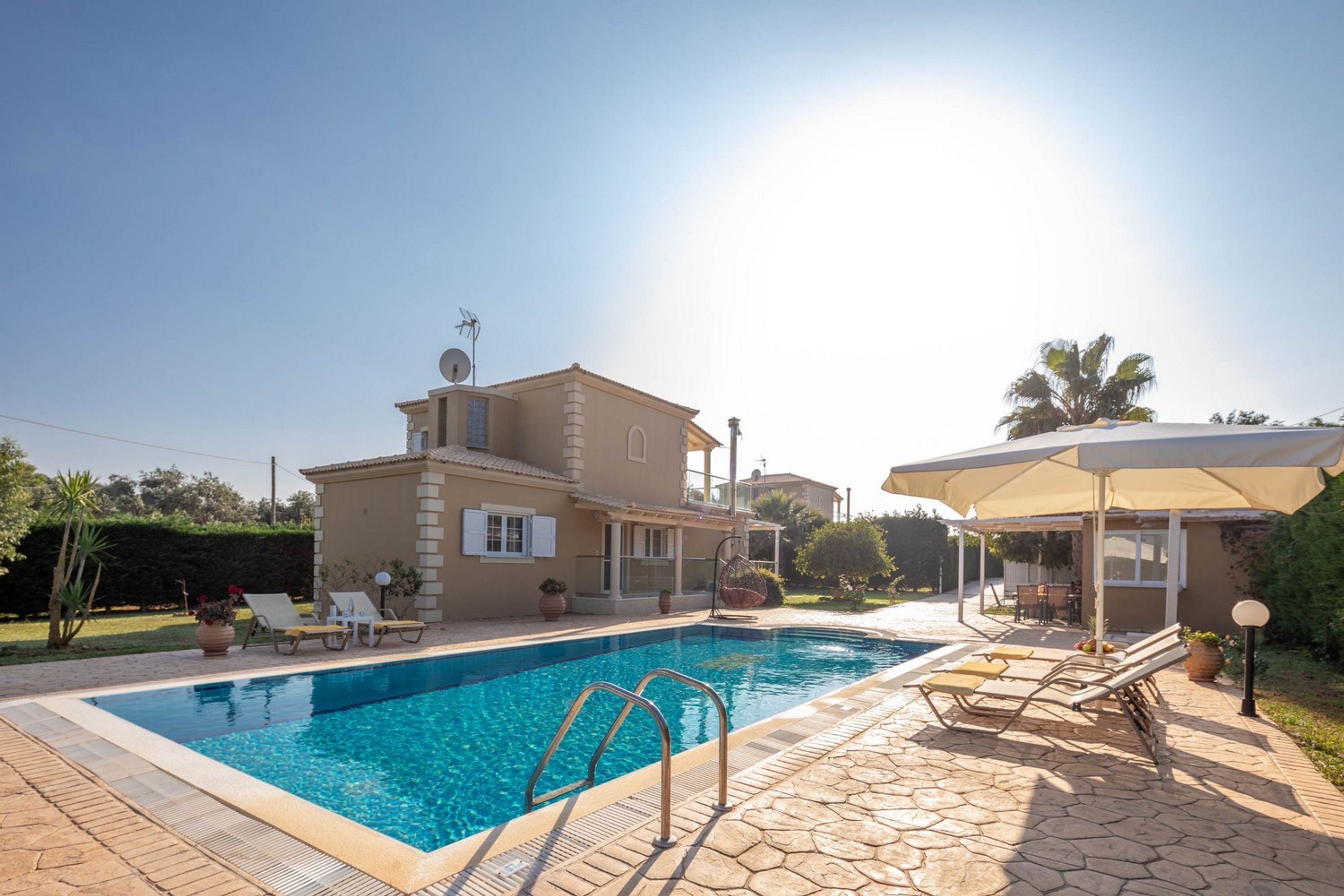 Un área de piscina con una casa, sillas de descanso y una pérgola.