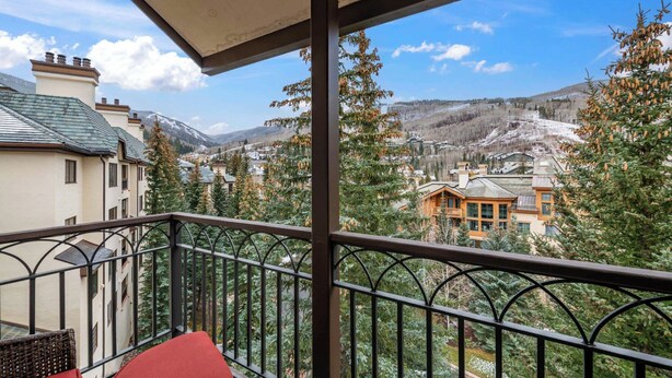 A balcony with a view of a mountainous landscape, a wooden building, and a tree with pine cones.