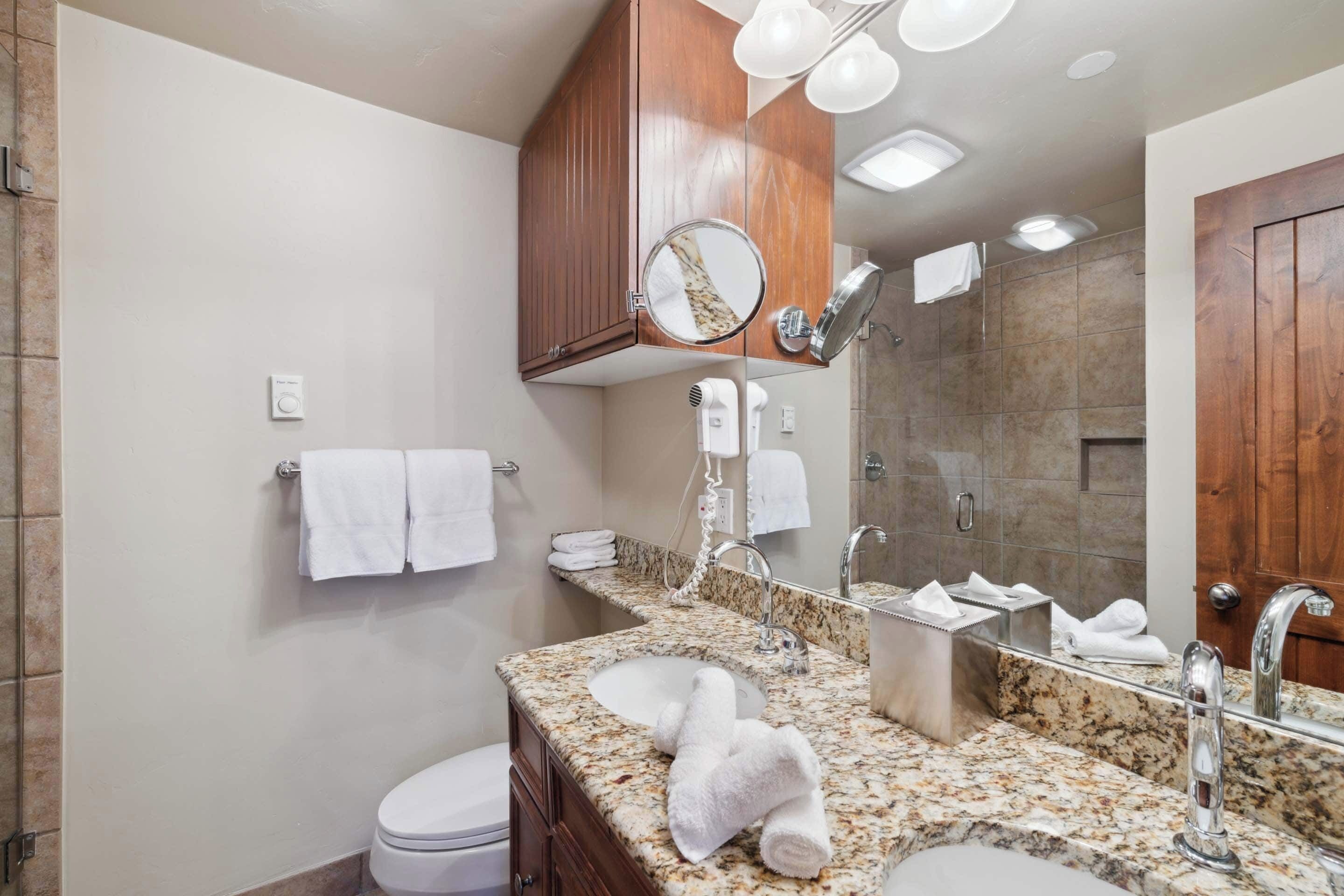A modern bathroom with a granite countertop, a sink, a toilet, a mirror, and a shower area.