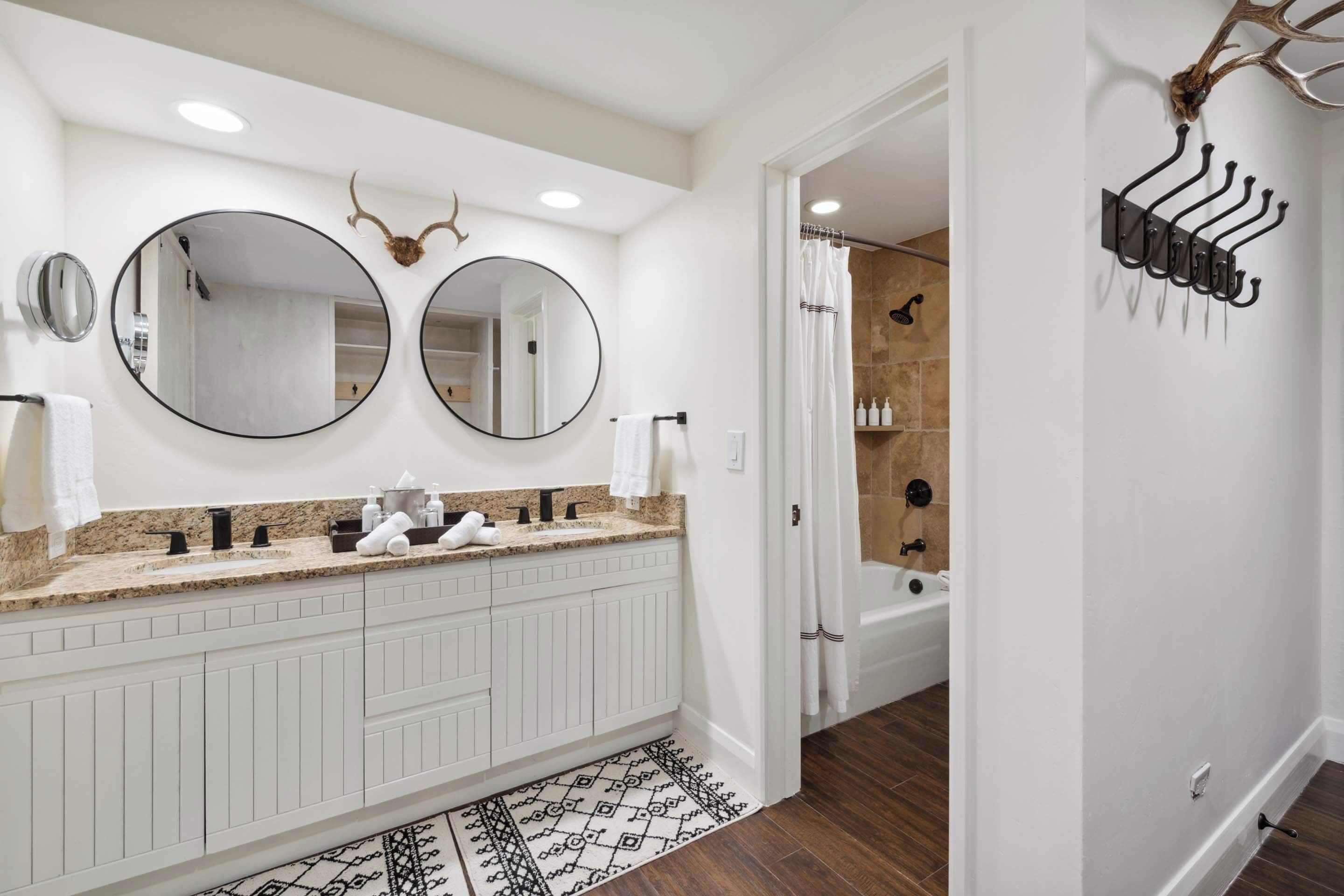 A modern bathroom with a double vanity, two mirrors, a shower, and a towel rack.
