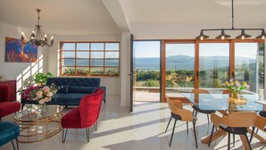 A spacious living room with a blue sofa, red chairs, a glass coffee table, and a dining area with a glass table and chairs. - Luxury Villa with big private swimming pool surrounded by forest and wineyards (Imotski)