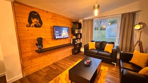 A living room with a wooden wall, a black leather sofa, a coffee table, and a television mounted on the wall. - Spacious Sheffield Lodge (Sheffield)