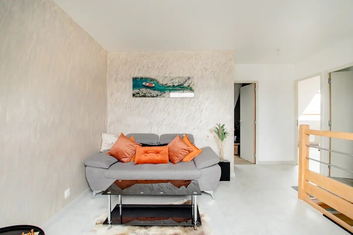 Ein modernes Wohnzimmer mit einem grauen Sofa, orangefarbenen Kissen, einem Couchtisch und einem Gemälde einer Flusslandschaft.