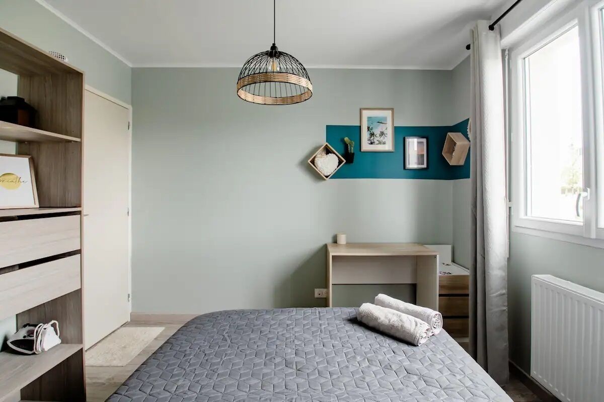 A bedroom with a bed, a desk, a wardrobe, and a hanging light fixture.