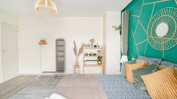 A modern bedroom with a bed, a standing lamp, a shelf with decorative items, and a geometric wall design.