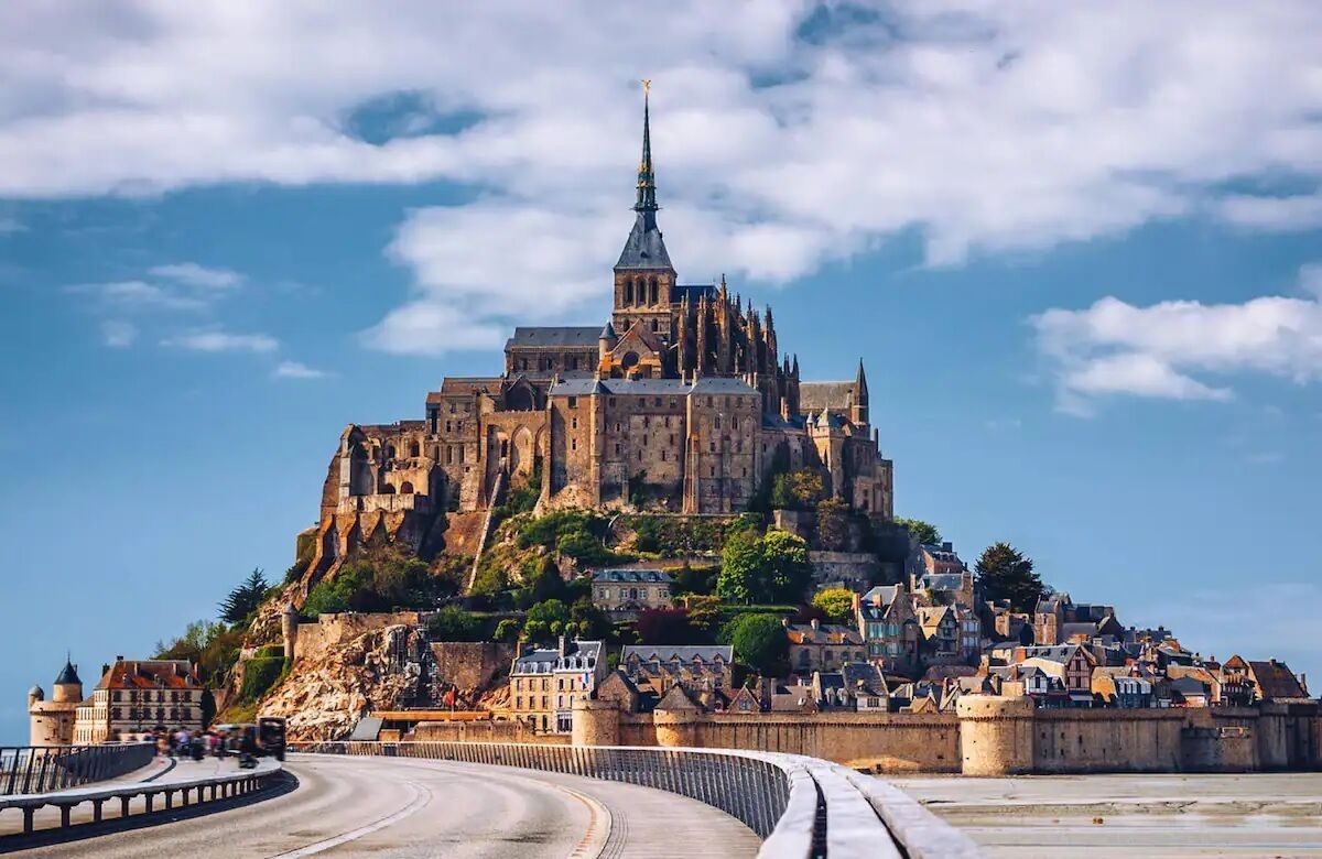 A historic castle with a prominent tower, situated on a hill overlooking a coastal town.