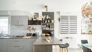 A modern kitchen with grey cabinets, a central island, and a dining area with a glass table and bar stools. - Casa Mogador 10 min from Saint Malo! ideal for families  (Miniac-Morvan)