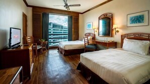A hotel room with a bed, a desk, a chair, a television, a ceiling fan, and a window with a view of buildings. - Sabah Oriental Hotel Kota Kinabalu (Kota Kinabalu)