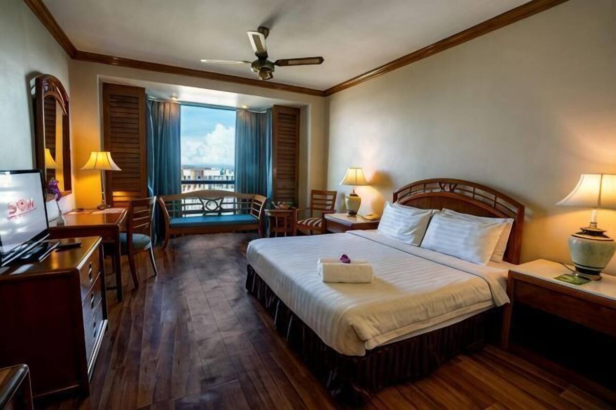 A hotel room with a bed, desk, chair, TV, and a balcony view.
