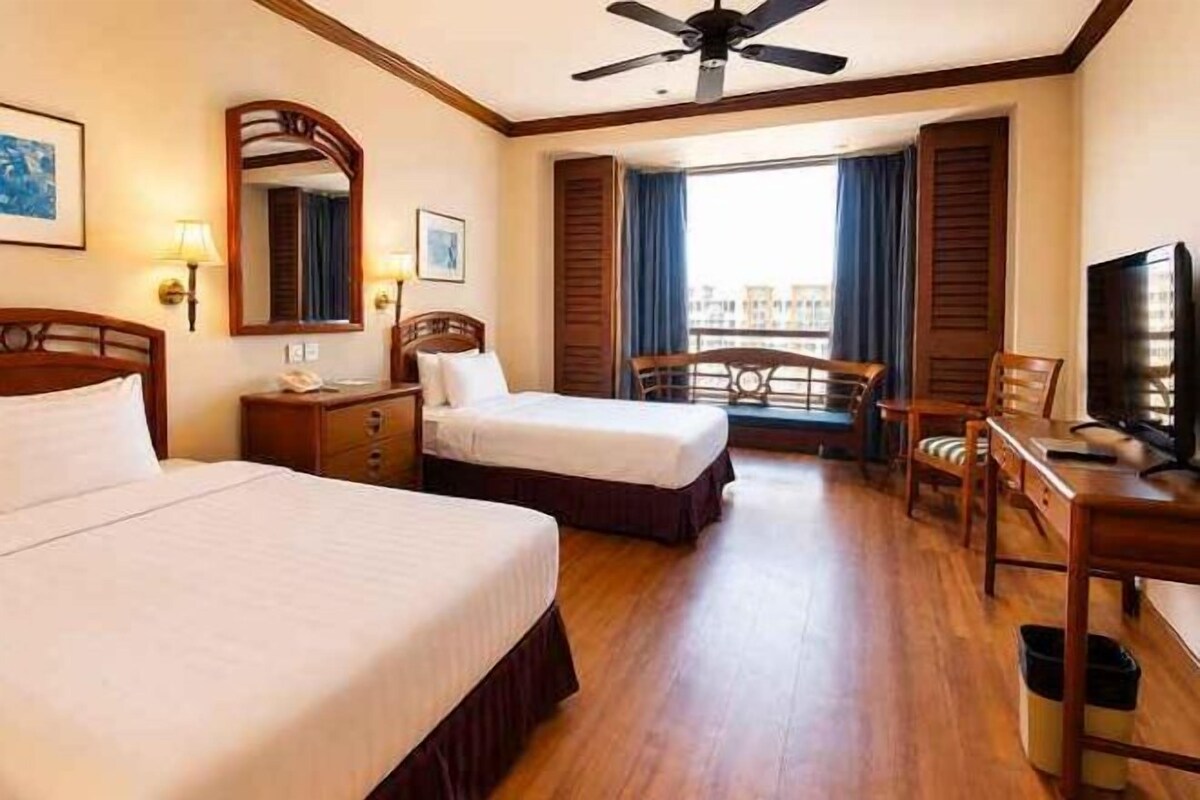 A hotel room with two beds, a desk, a chair, a television, and a ceiling fan.