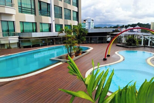Una piscina con cubierta de madera, rodeada de plantas en macetas y baranda de cristal.
